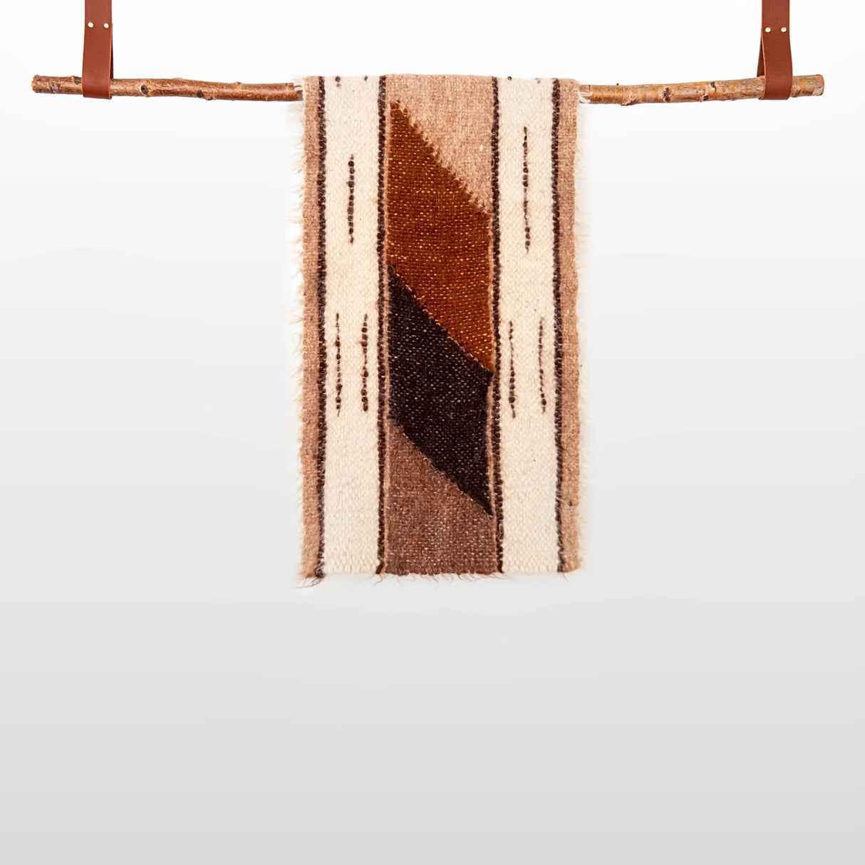 The Tak (Yes) Wool Bed / Couch Runner, featuring a brown and cream geometric handwoven design, hangs elegantly from a wooden rod with leather straps—perfect for sustainable home decor.