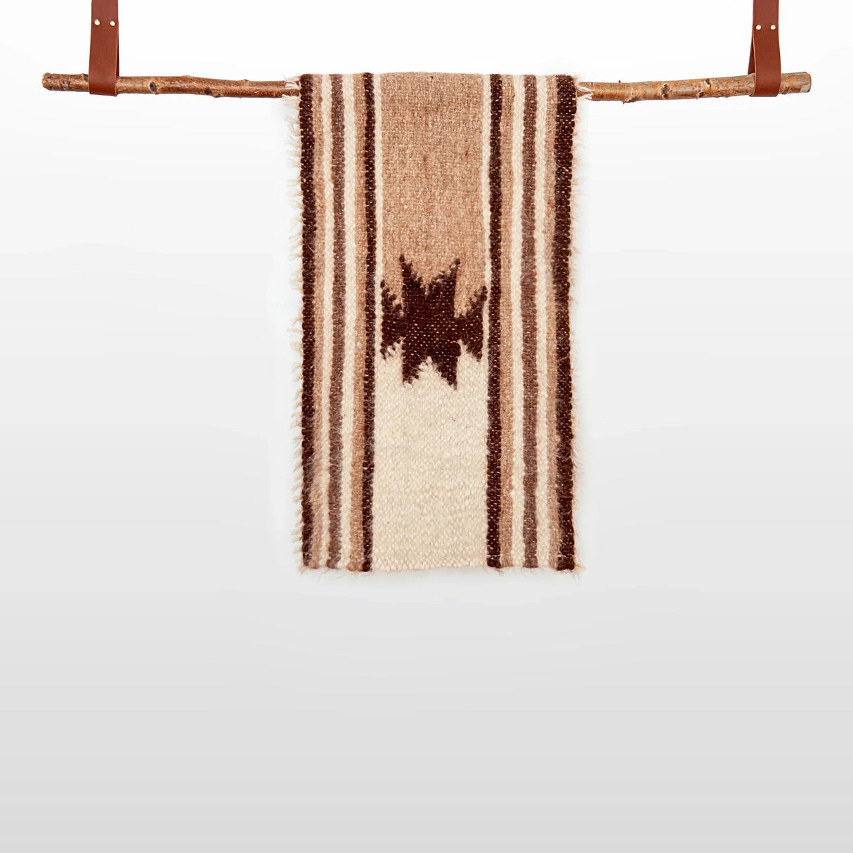 The Opora (Pillar) Wool Bed/Couch Runner, handwoven with brown stripes and a central star plus subtle Carpathian motifs, hangs on a wooden rod with leather straps.
