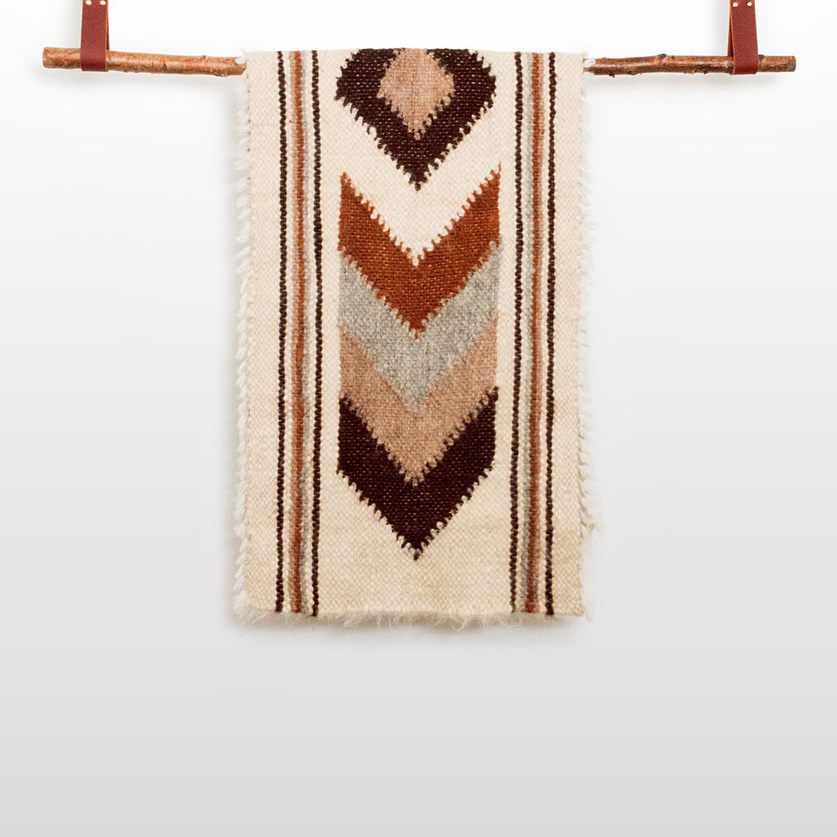 The Tkach (Weaver) Wool Bed / Couch Runner features chevron patterns in brown, tan, and cream, crafted from virgin undyed wool and inspired by traditional Tkach blanket designs, draped elegantly over a wooden rod.