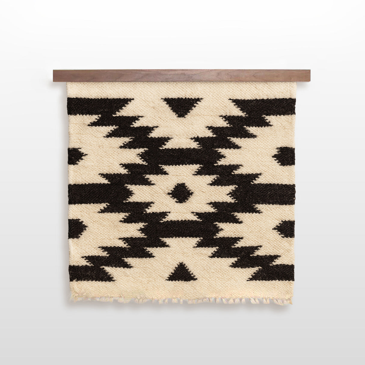 The Zytia (Life) Wool Wall Hanging features a beige woven design with handcrafted wool zigzags and striking black diamond patterns, all displayed on a wooden rod.