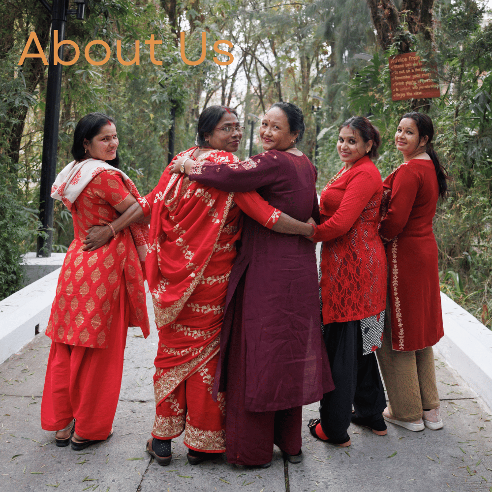 Five women in colorful outfits stand side by side, smiling and posing outdoors in a lush, green setting.