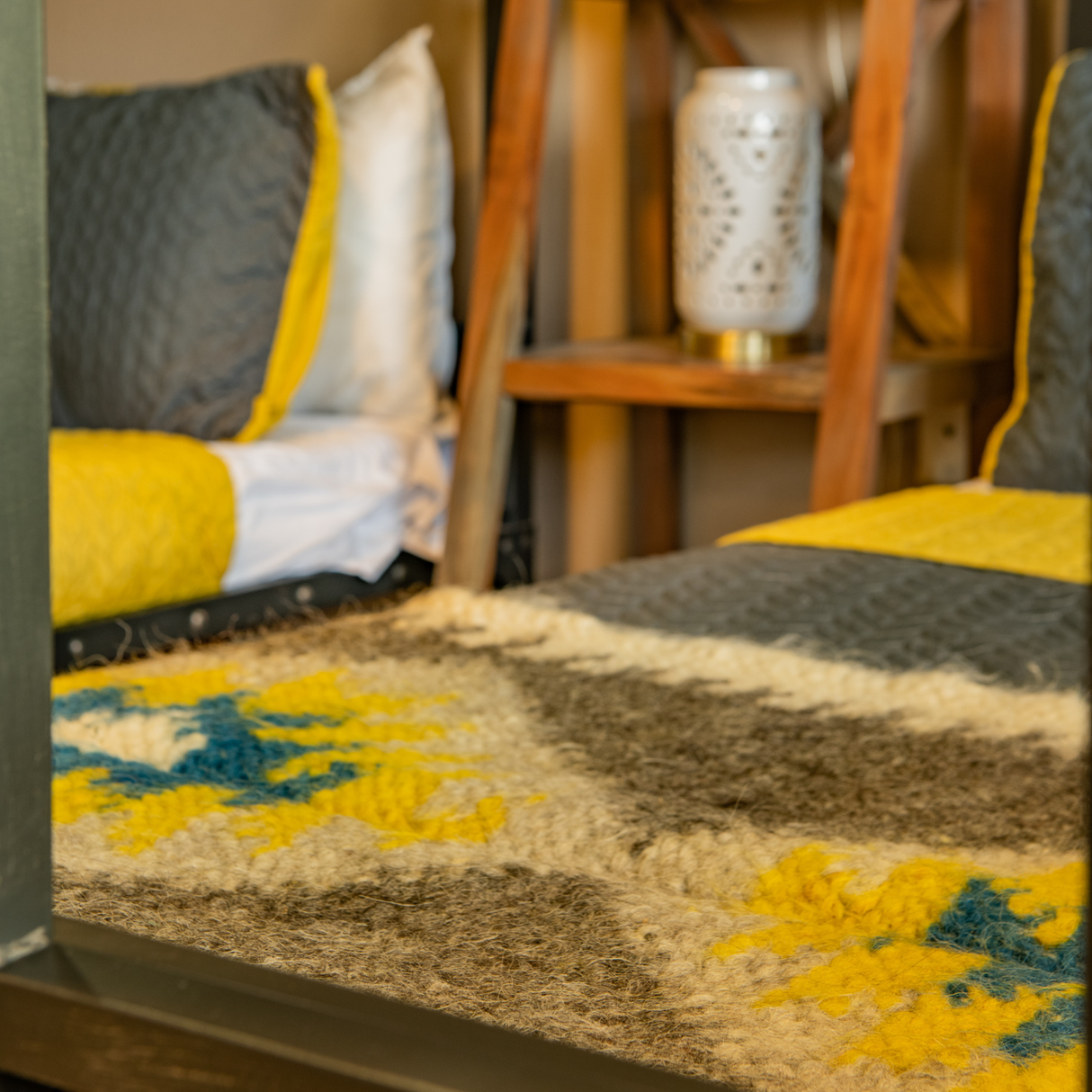 Close-up of a cozy bedroom with a yellow and gray bed topped by the Organic 100% Sheep Wool Bed Runner—Handmade Ukrainian Couch Cover or Bedspread from the Carpathian Mountain Collection, highlighting artisan craftsmanship.