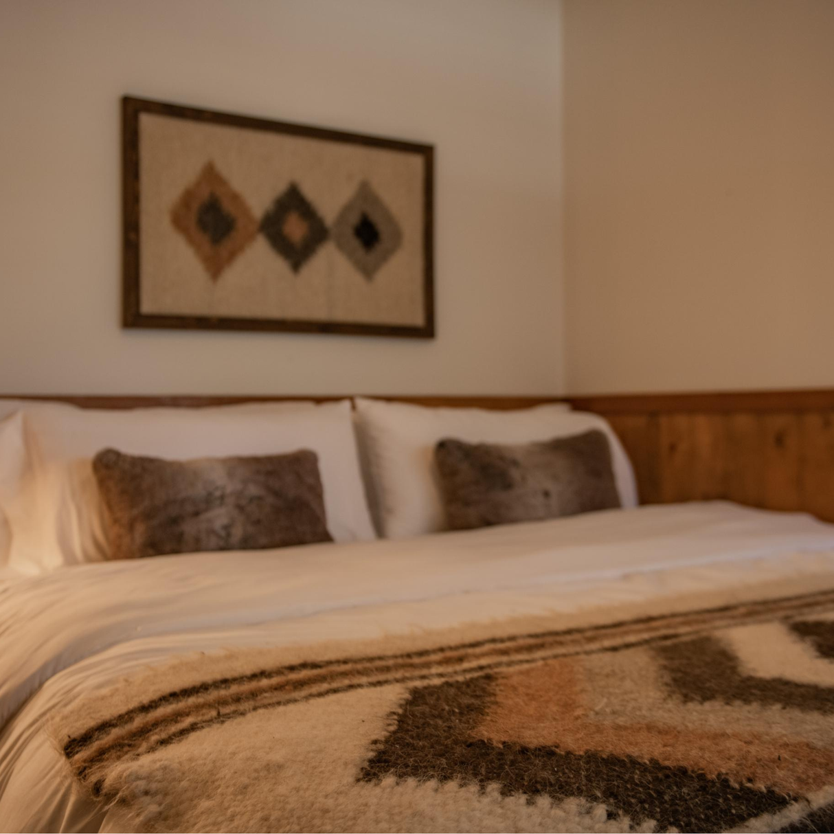Cozy bed with white linens, fur pillows, and a geometric blanket, complemented by the Harny (Beautiful) Wool Framed Wall Art above the headboard.