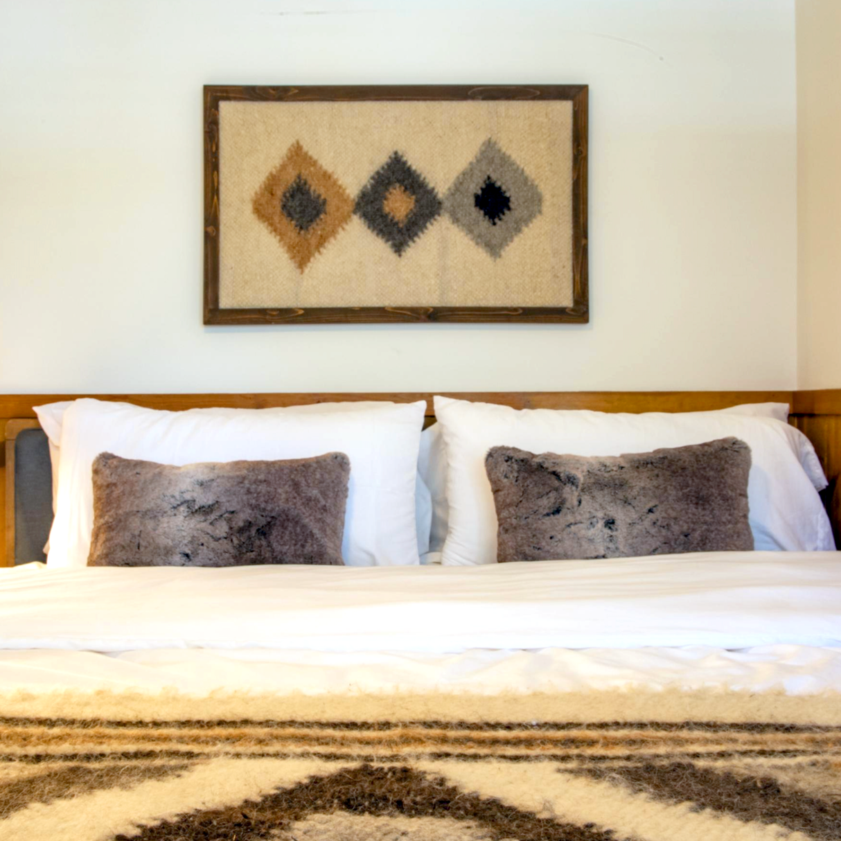 Cozy bed with two gray pillows, featuring the Harny (Beautiful) Wool Framed Wall Art with abstract diamond patterns hanging above the headboard.