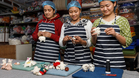 Three women in striped aprons make felt animal crafts at a table, surrounded by colorful supplies.