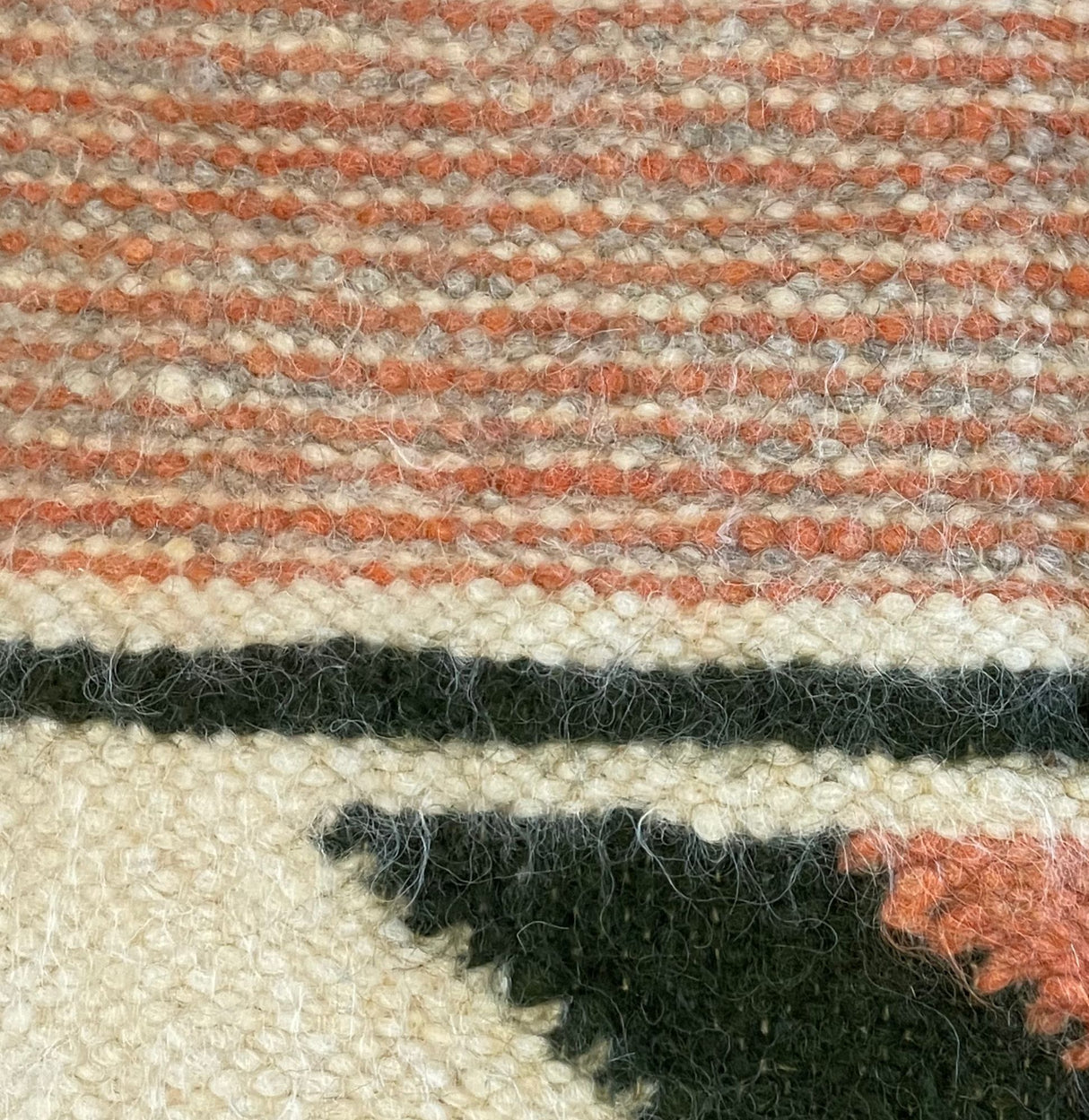 Close-up of a Handmade Organic 100% Sheep Wool Woven Statement Blanket, featuring geometric patterns in cream, pink, black, and reddish tones—an eco-friendly bed covering that highlights sustainable craftsmanship.