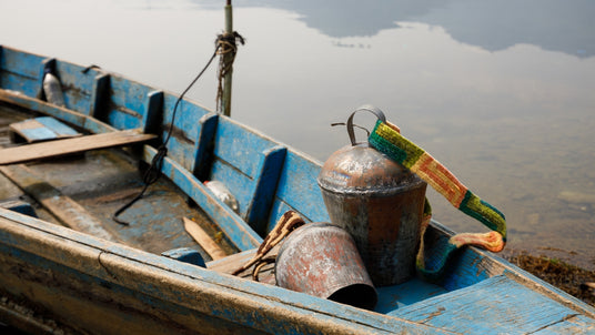 Weathered blue wooden boat with metal buckets and a colorful strap, floating on calm water.