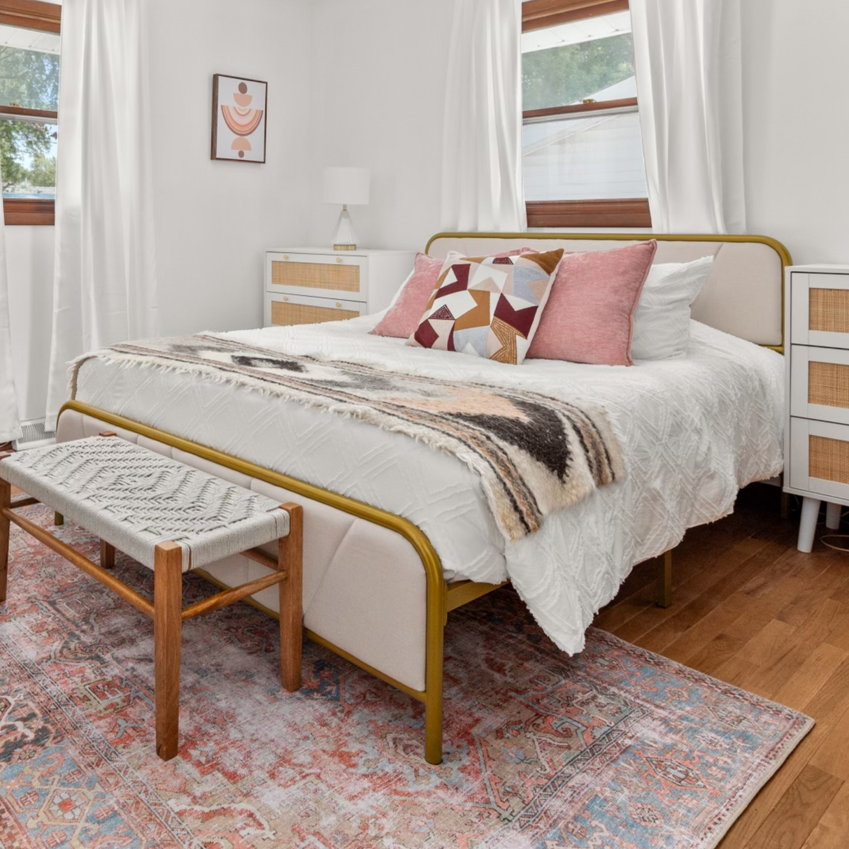 Bedroom featuring a stylish bed, patterned pillows, a handcrafted Tkach (Weaver) Wool Bed/Couch Runner, a bench, white curtains, and a colorful rug on the wooden floor.