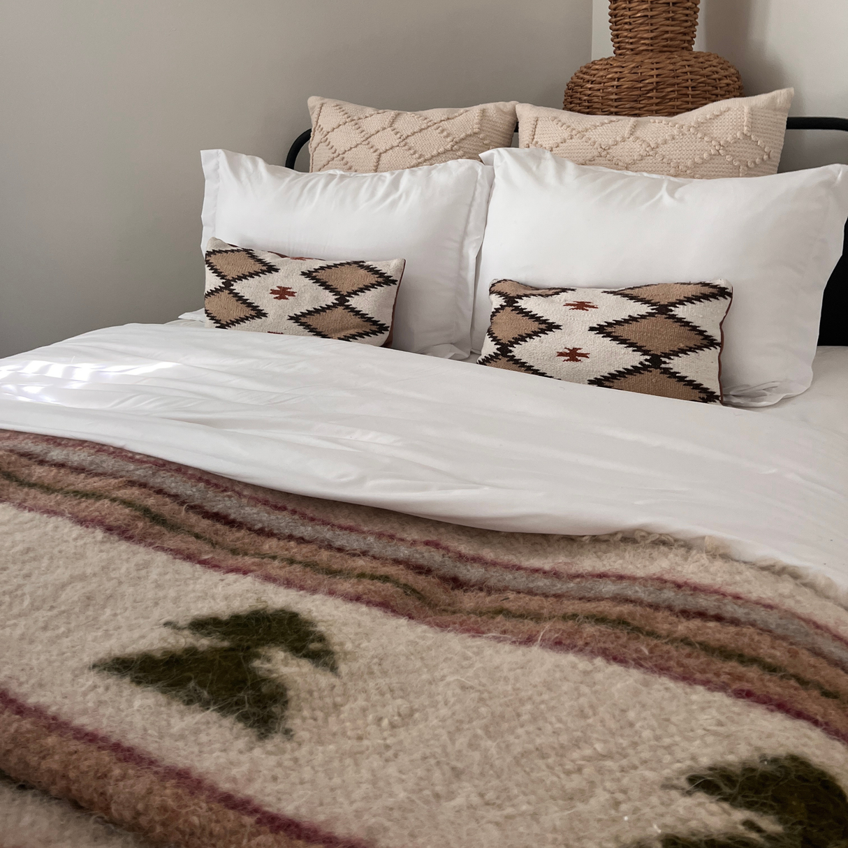 A neatly made bed with white pillows, patterned cushions, and a cozy Sosna (Pine) Wool Statement Bed Blanket featuring tree designs.