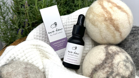 A bottle of "Ewe Dew" Lavender Rain oil with box, surrounded by wool dryer balls and lavender.