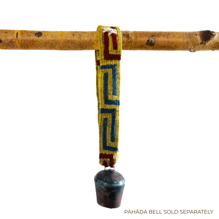 A Large Strap for Hanging Vintage Bells, featuring a yellow, red, and blue handcrafted pattern, suspends a small metal bell from a wooden rod.