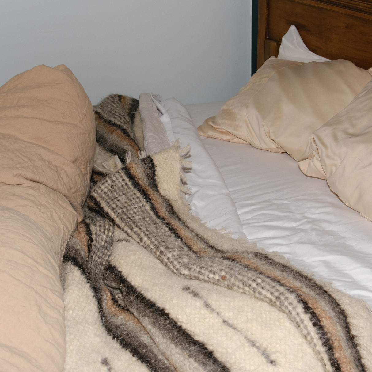 Unmade bed with beige pillows and a Gratsia (Grace) Wool Statement Bed Blanket lying on white sheets, creating a cozy and stylish look.