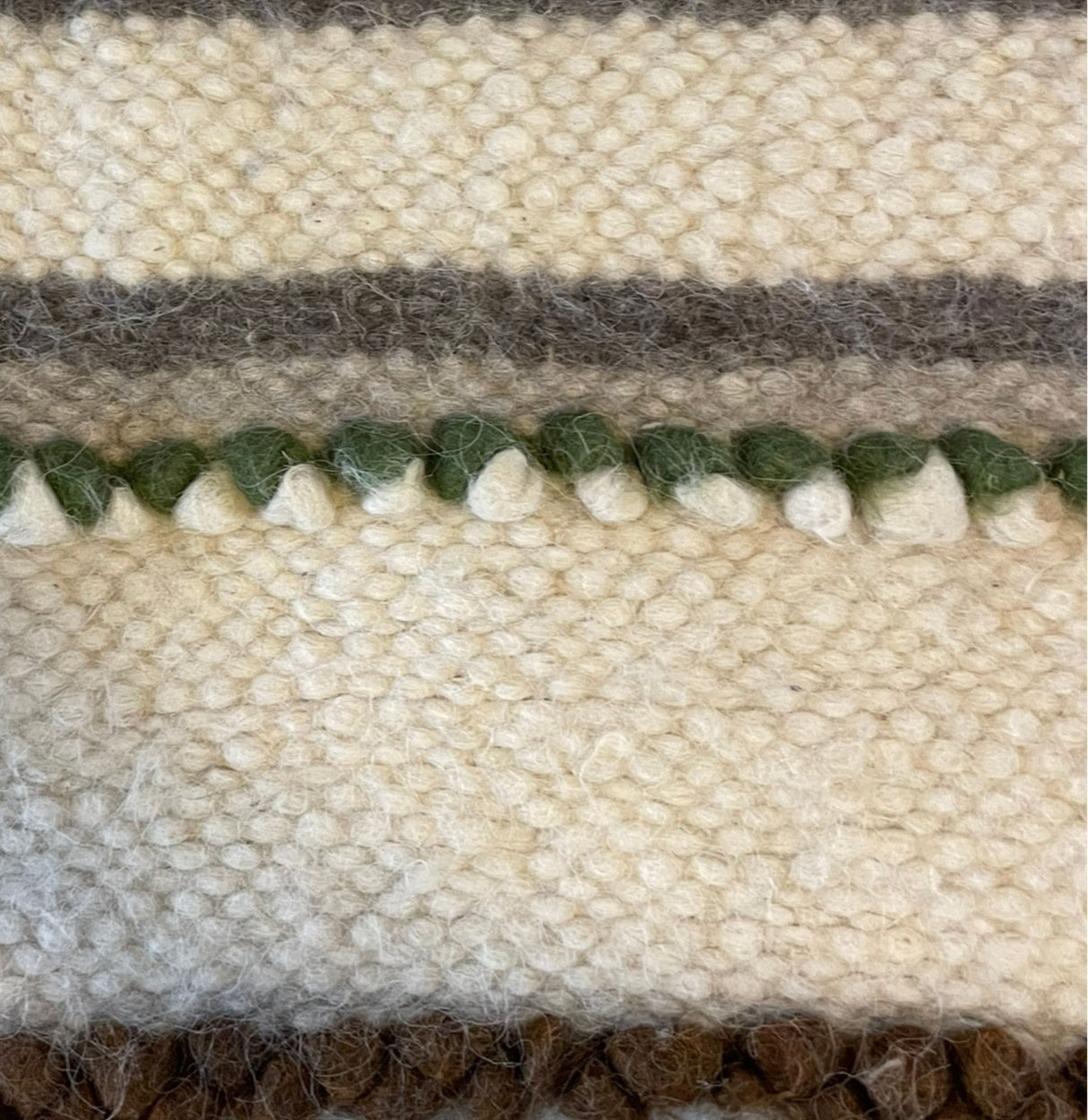 Close-up of the Faino (Fine) Wool Statement Bed Blanket, featuring white, green, brown, and gray yarn in textured horizontal stripes—a handcrafted piece that brings artisanal charm to any room.