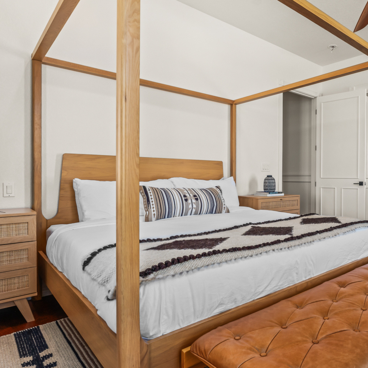 A modern bedroom with a wooden canopy bed, white bedding, and a tan bench, accented by a handcrafted Korysno Wool Bed / Couch Runner made from 100% virgin wool.