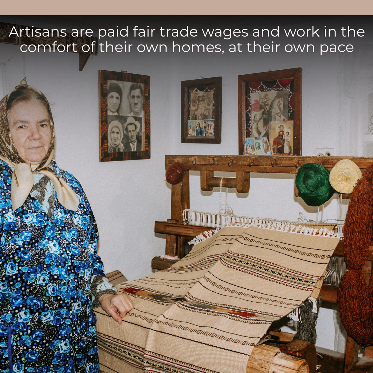 An older woman in a patterned dress weaves a Wool Table Runner at home on a loom, with photos and yarn displayed behind her.