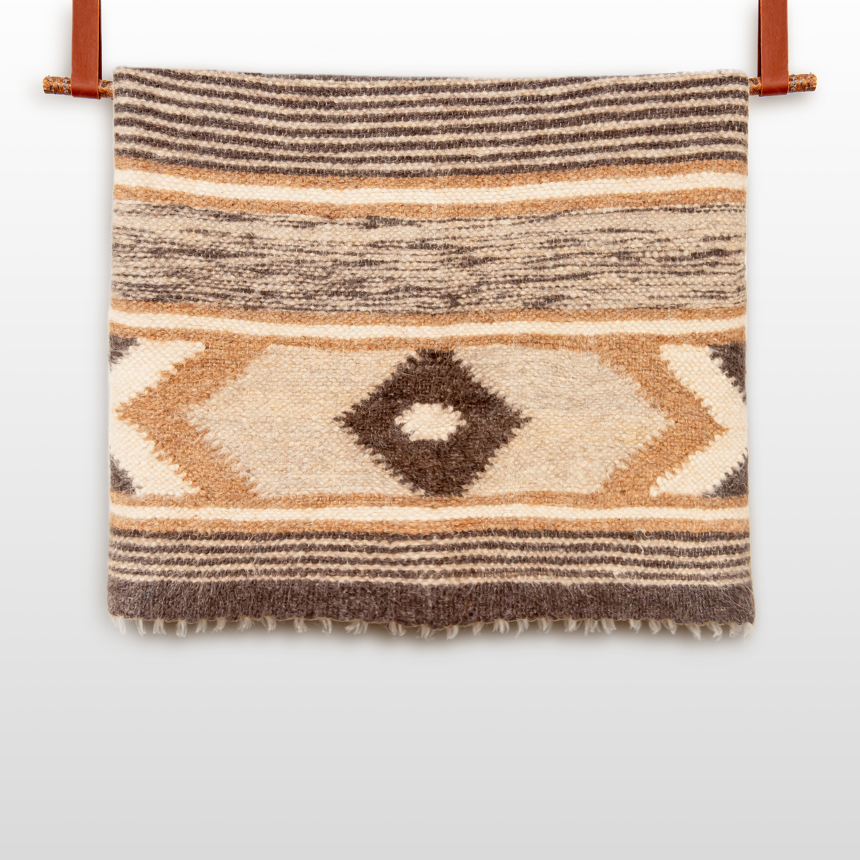 The Peremoha (Victory) Wool Statement Bed Blanket features brown, beige, and cream geometric patterns and hangs from two leather straps, adding a cozy touch to any space.