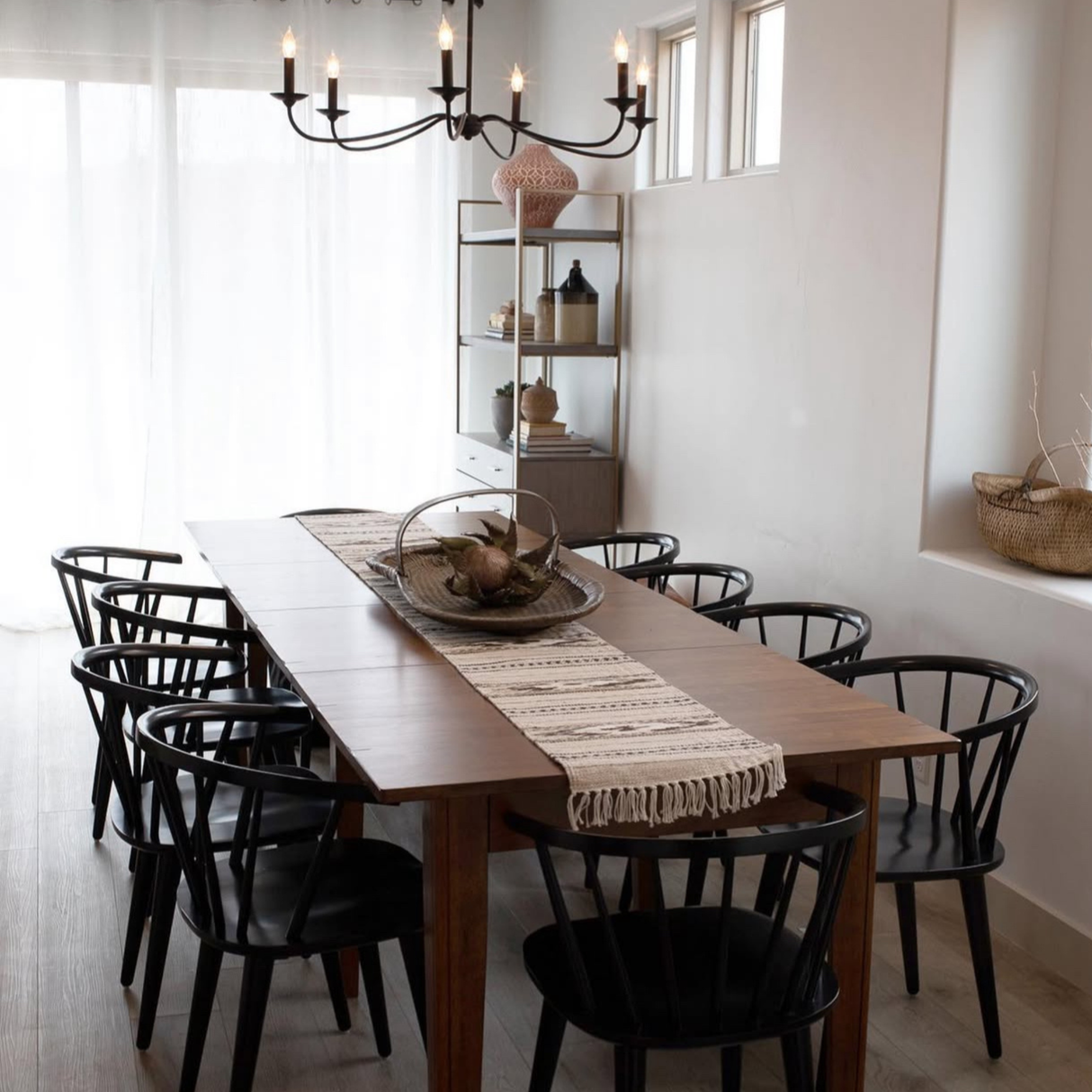Modern dining room with a wooden table featuring a Wool Table Runner, black chairs, a chandelier, and minimalist decor.