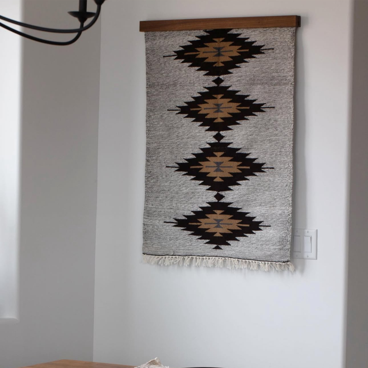 The Smilyv Wool Rug / Wall Hanging features geometric diamond patterns in black and brown on white, styled for eco-friendly décor. Includes a wood rug hanger.