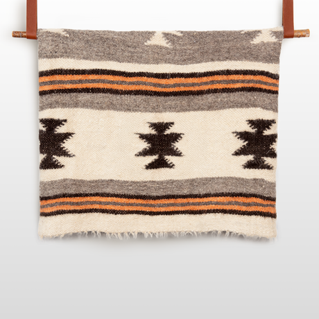 The Chysto (Pure) Wool Statement Bed Blanket is hand woven with brown, orange, and cream stripes, geometric patterns, and subtle Ukrainian star motifs, shown hanging on a wooden rod.