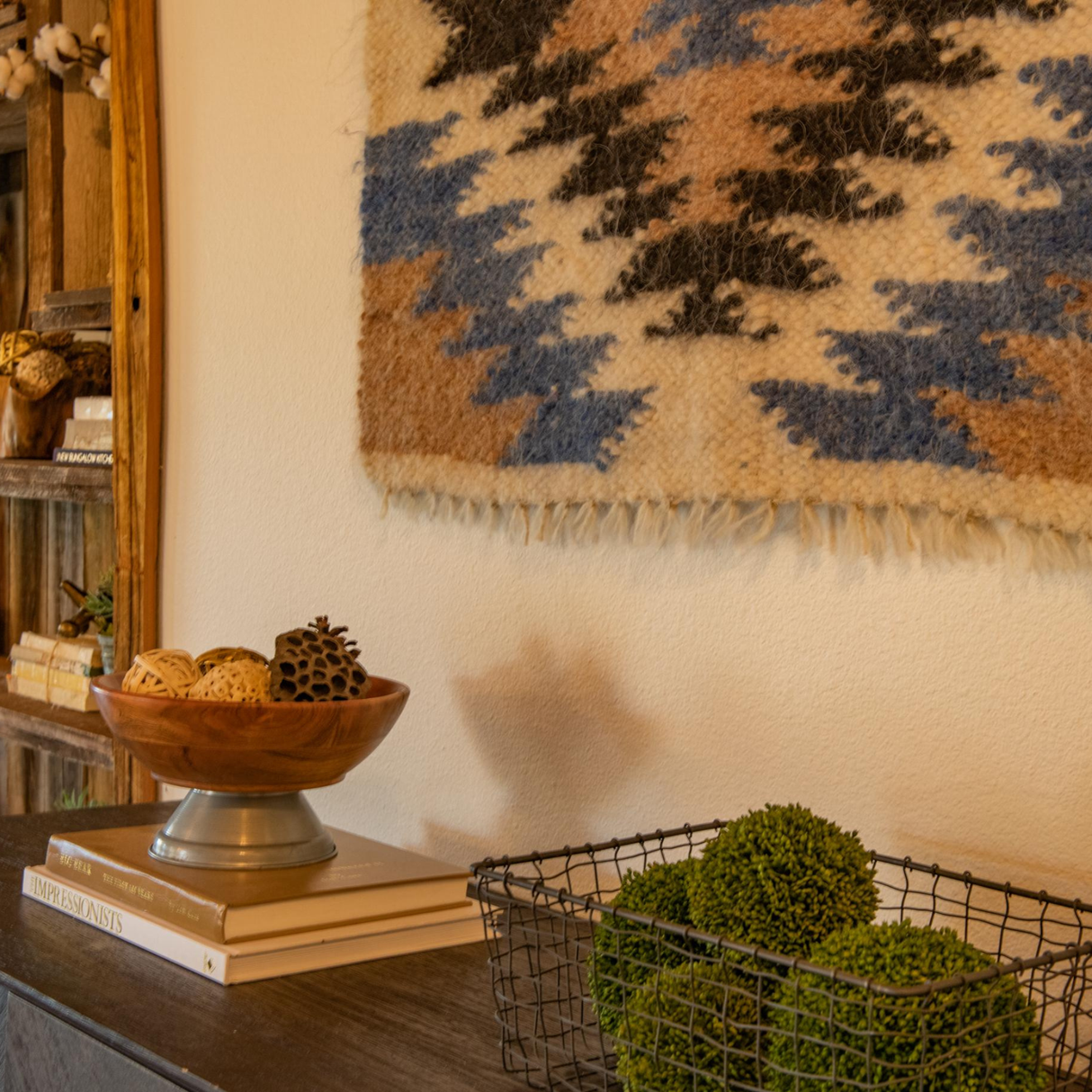 A decorative bowl and wire basket sit on the table, while the Zirka (Star) Wool Wall Hanging, handcrafted from Carpathian sheep wool, is displayed above on the patterned rug.