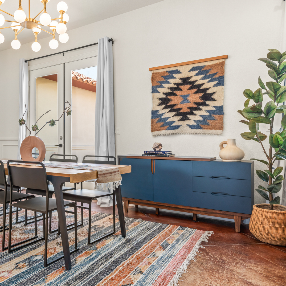 Dining room with modern decor, blue sideboard, patterned rug, plant, and geometric wall art featuring the handcrafted Zirka (Star) Wool Wall Hanging inspired by Carpathian sheep wool.