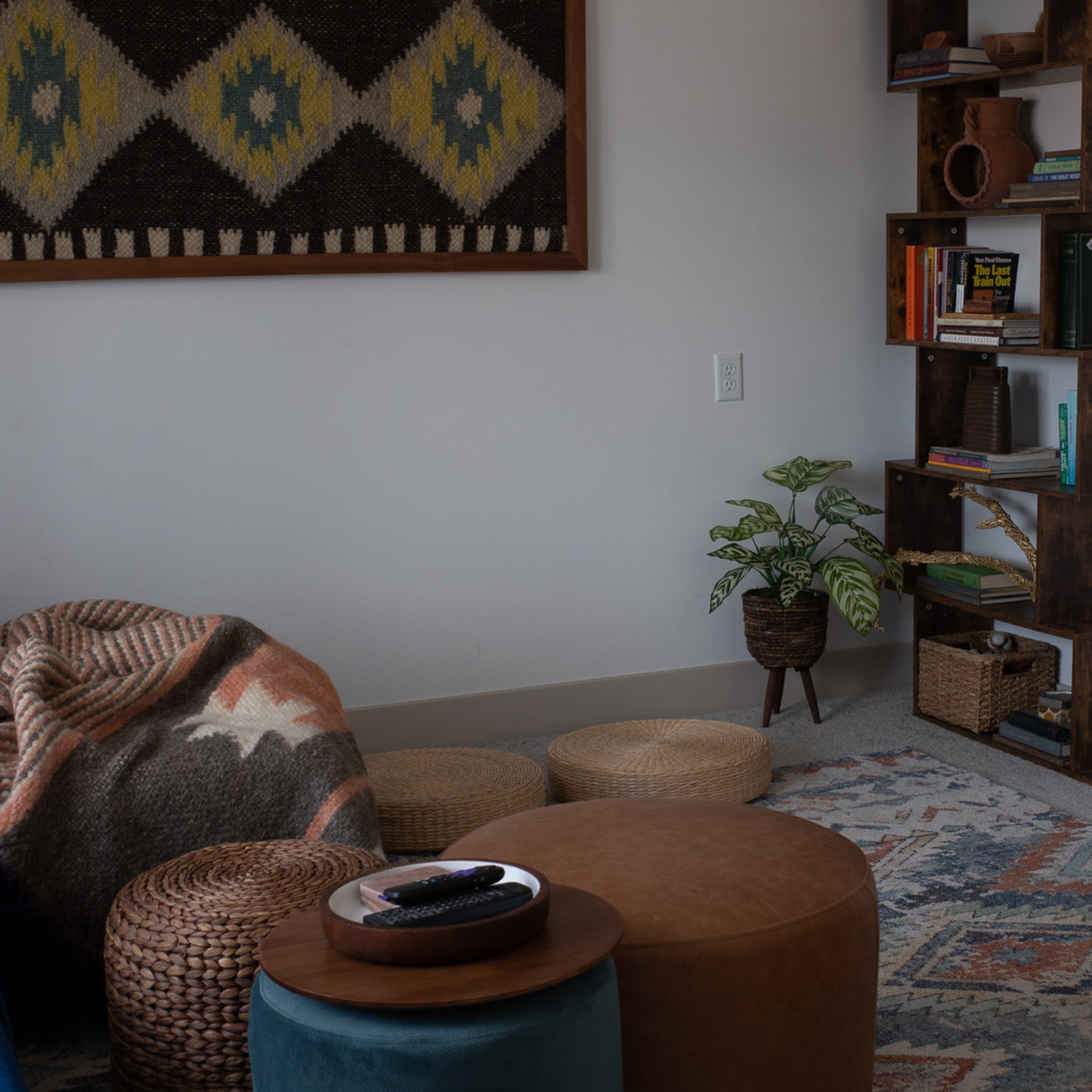 Cozy living room with poufs, a plant, bookshelves, and a patterned blanket draped over a chair, complemented by the handcrafted Mriya (Dream) Wool Wall Hanging for added warmth and charm.