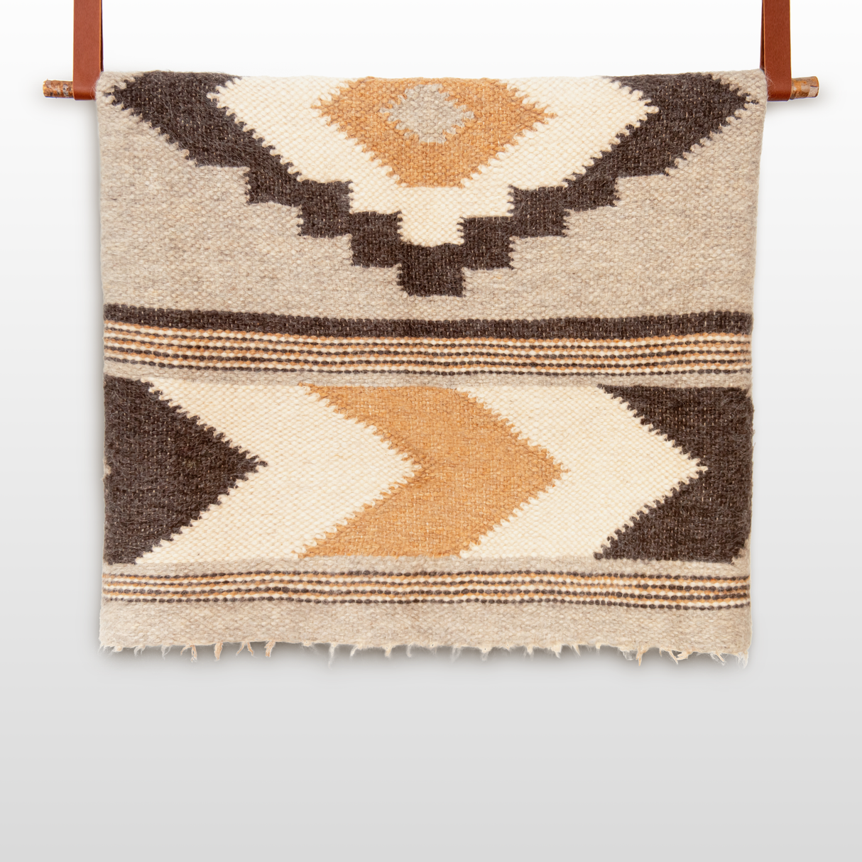 The Myr (Peace) Wool Statement Bed Blanket features handcrafted geometric patterns in brown, tan, and cream, made from undyed yarn and displayed on a leather rod.