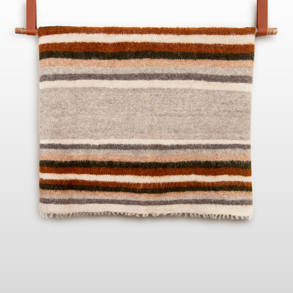 The Mudry (Wise) Wool Statement Bed Blanket, featuring brown, orange, gray, and cream stripes, is folded and displayed on a wooden rod.