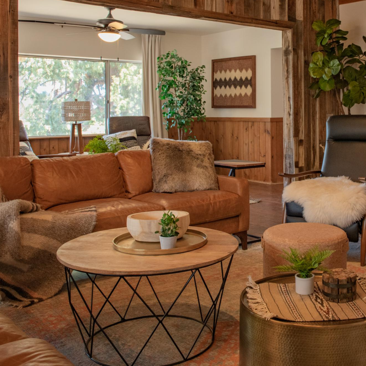 Warm, cozy living room with brown leather sofas, artisanal decor, potted plants, and wooden accents. The Dobre (Good) Wool Framed Wall Art adds a touch of modern charm with its geometric design.