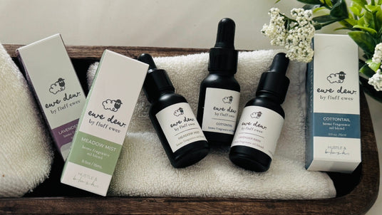 Three dropper bottles and two boxes of "Ewe Dew by fluff ewes" essential oils on a towel with flowers.