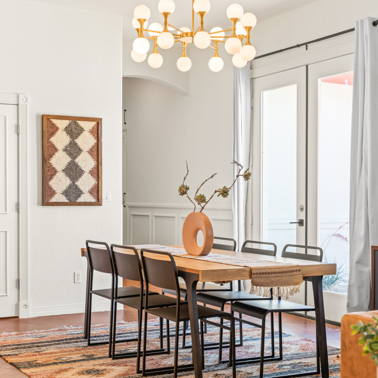 A modern dining room with a wooden table, six chairs, a vase, and a geometric chandelier overhead is complemented by the Dobre (Good) Wool Framed Wall Art, adding texture and warmth to the space.
