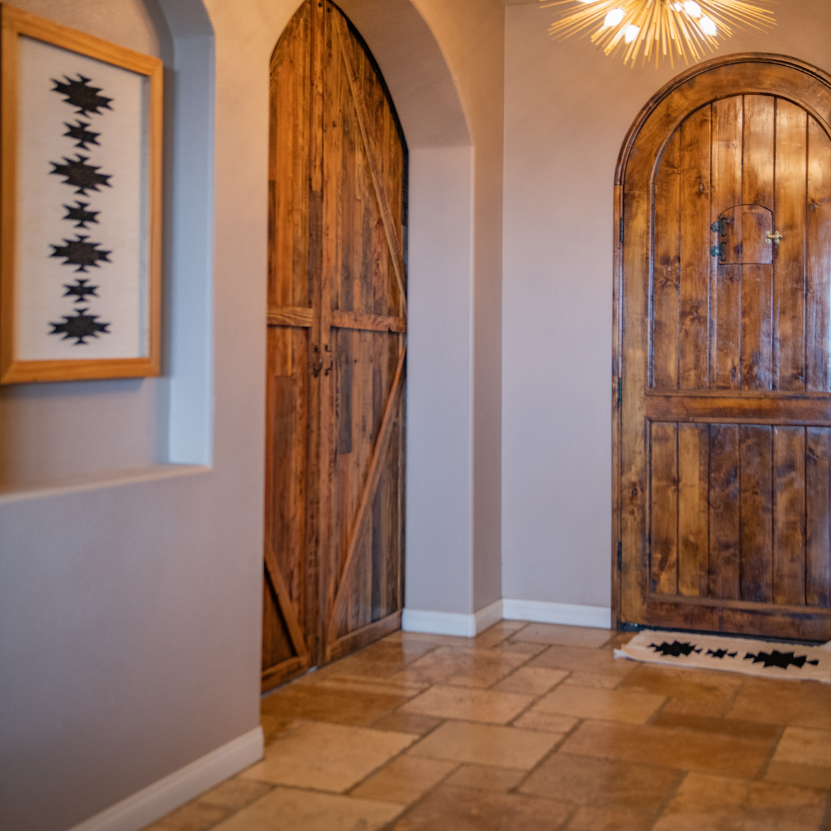 A hallway featuring a Chysto (Pure) Wool Rug as a wall hanging with a Hemlock Wood Rug Hanger, tan tile floor, and framed abstract art.