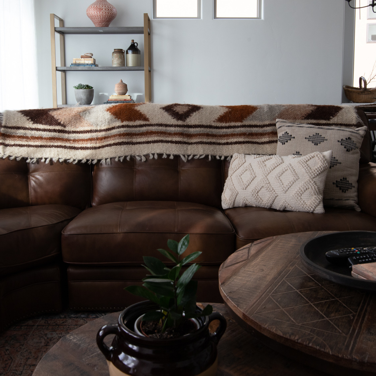 Brown leather sofa with a Tkach (Weaver) Wool Bed / Couch Runner, matching cushion, wooden coffee table, and a decorative shelf in the background.