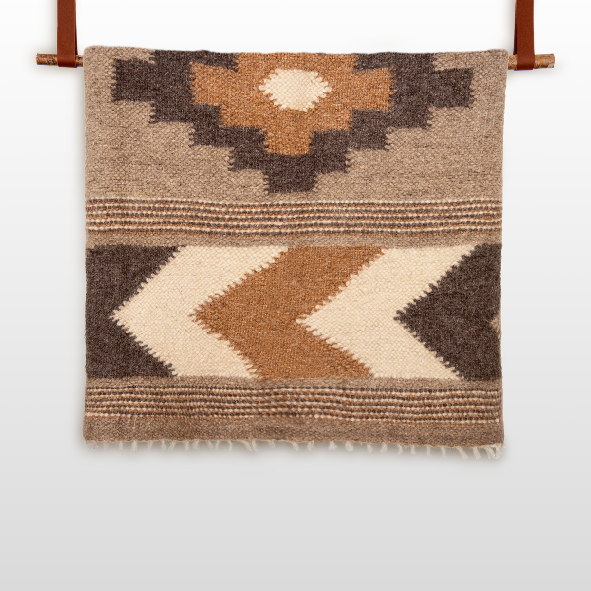 The Myr (Peace) Wool Statement Bed Blanket features a bold rhombus-dot design in brown, tan, and cream. Crafted from all-natural undyed yarn, it hangs on a rod with leather straps to add geometric flair to any space.