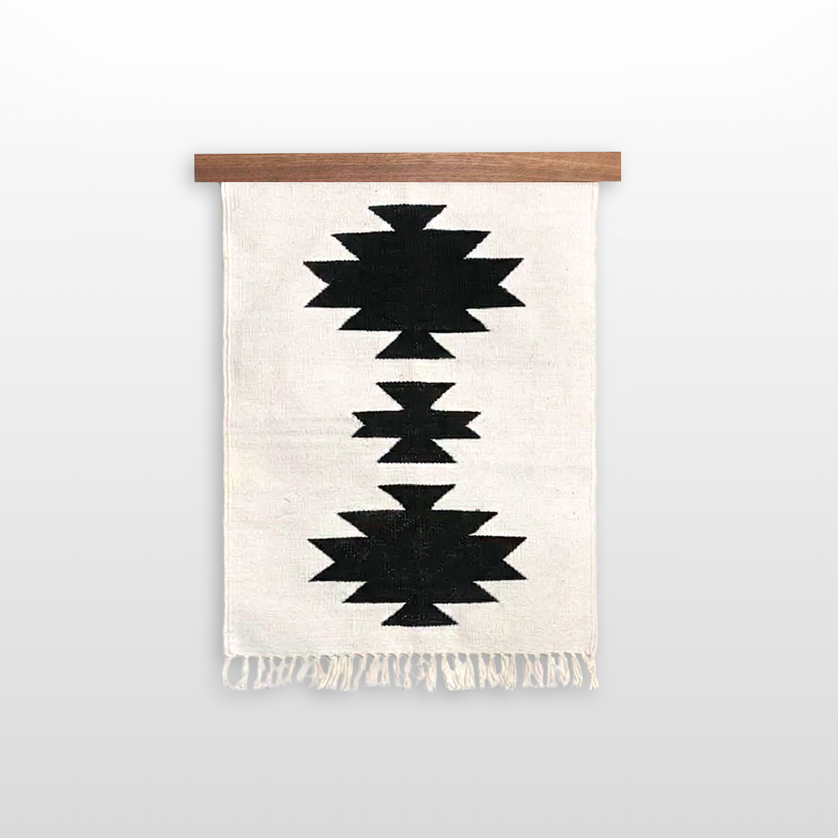 Handmade in Ukraine, this organic 100% sheep wool woven wall hanging features a black geometric design on white with fringe, inspired by the Carpathian Mountain collection and displayed on a wooden rod.