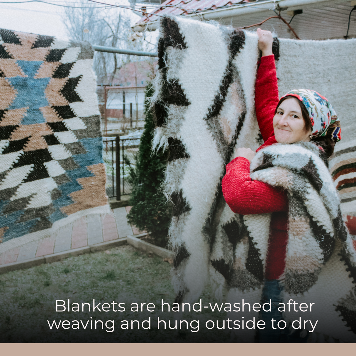 A smiling woman hangs the Myr (Peace) Wool Bed/Couch Runner, featuring a handcrafted rhombus-dot design, outside to dry on a clothesline.
