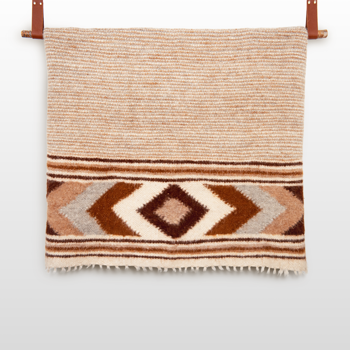 The Tkach (Weaver) Wool Statement Bed Blanket features brown, beige, and white geometric diamond patterns and is shown hanging on a wooden rod.
