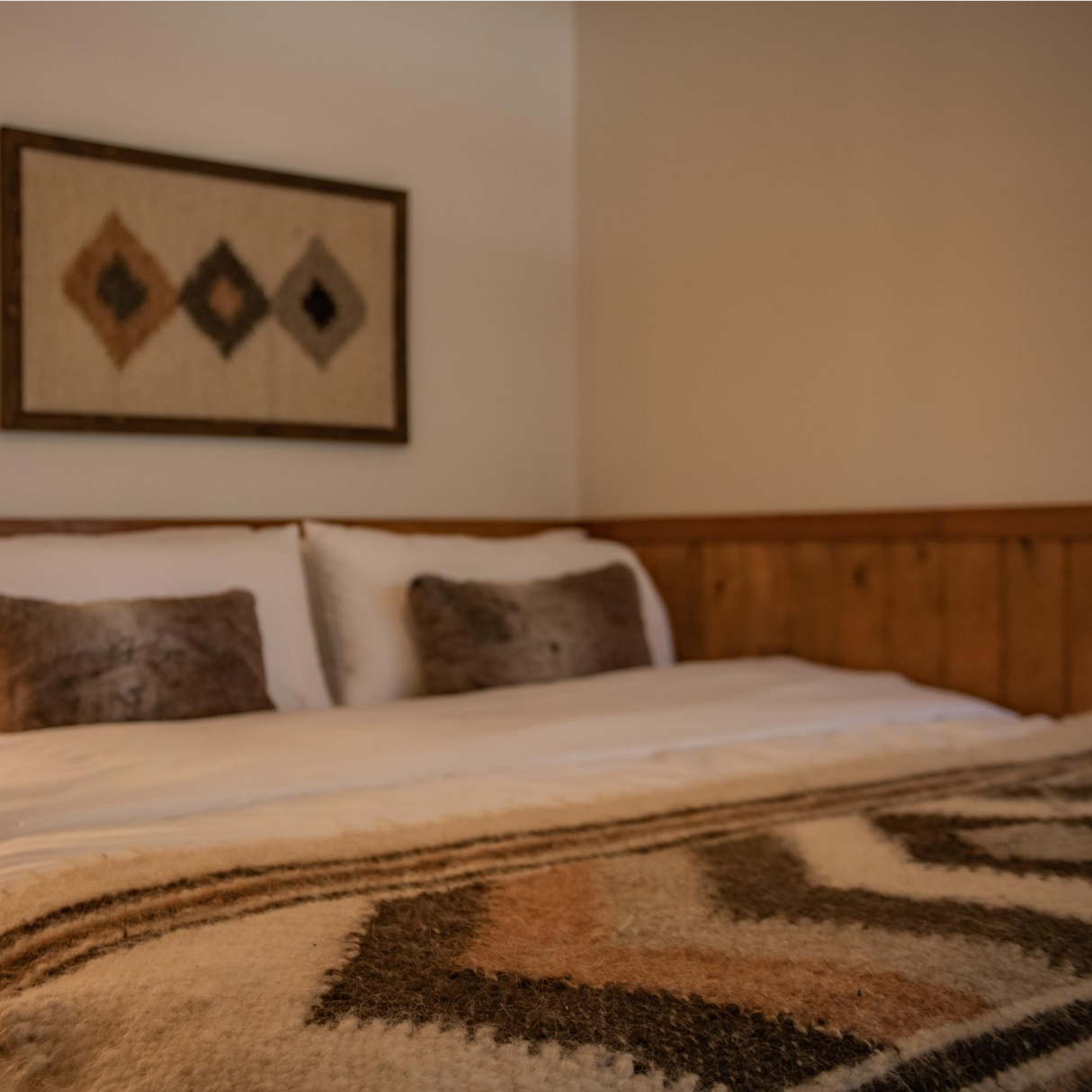 A warm, wood-paneled bedroom features a cozy bed with the Peremoha (Victory) Wool Statement Bed Blanket, two pillows, and wall art.