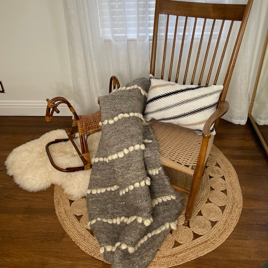 A wooden rocking chair with a pillow and the Vivtsi (Sheep) Wool Statement Throw / Baby Blanket beside a toy rocking horse on a round woven rug.