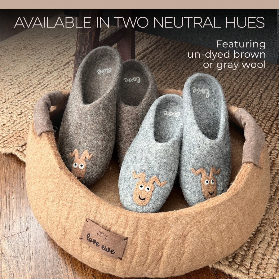 Two pairs of Love Ewe Hand-Felted Organic Wool Slippers for Men (Beau-G), in brown and gray with dog faces, are placed in a round tan pet bed on a woven rug.