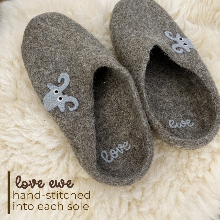 Love Ewe Hand-Felted Organic Wool Slippers for Men (Blu-B) feature cozy gray wool, a sheep design, and "love" hand-stitched into each sole—perfect fair trade comfort on a fluffy surface.