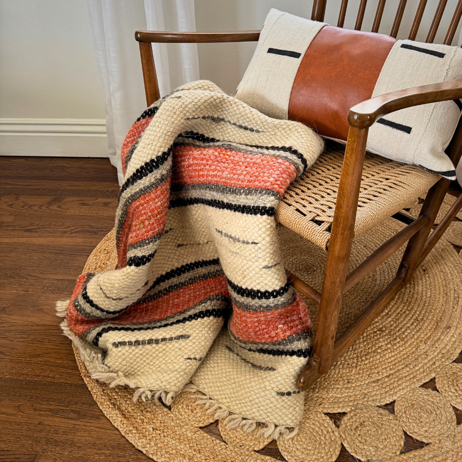 The Chudovo (Well) Wool Statement Throw / Baby Blanket, featuring red and black stripes and made from Carpathian sheep wool, is draped over a wooden chair with a cushion, resting on a round rug.
