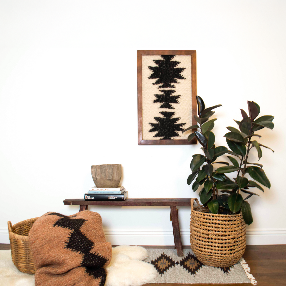Bench with woven baskets, books, a plant, and the Chysto (Pure) Wool Framed Wall Art, creating a cozy, eco-friendly vibe against a white wall.