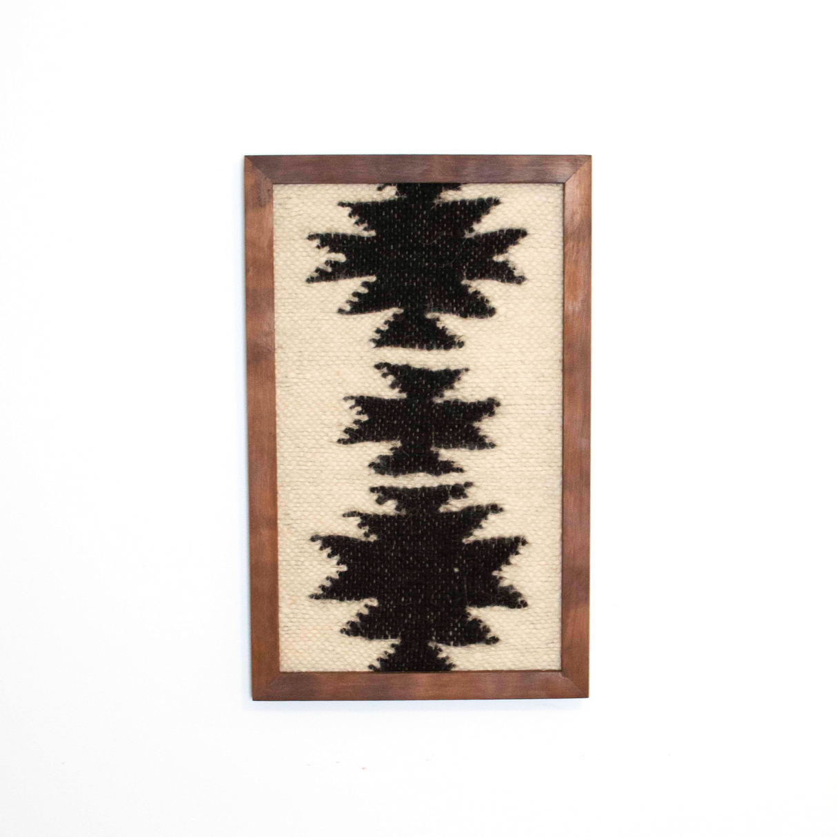 The Chysto (Pure) Wool Framed Wall Art features black geometric shapes on a beige background, handcrafted in a rectangular frame and displayed on a white wall.