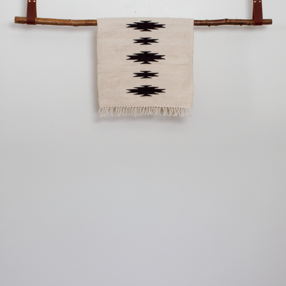 The Chysto (Pure) Wool Rug / Wall Hanging features black geometric patterns and hangs on a wooden rod against a plain white wall, offering a bold art statement perfect for the modern sophisticate.