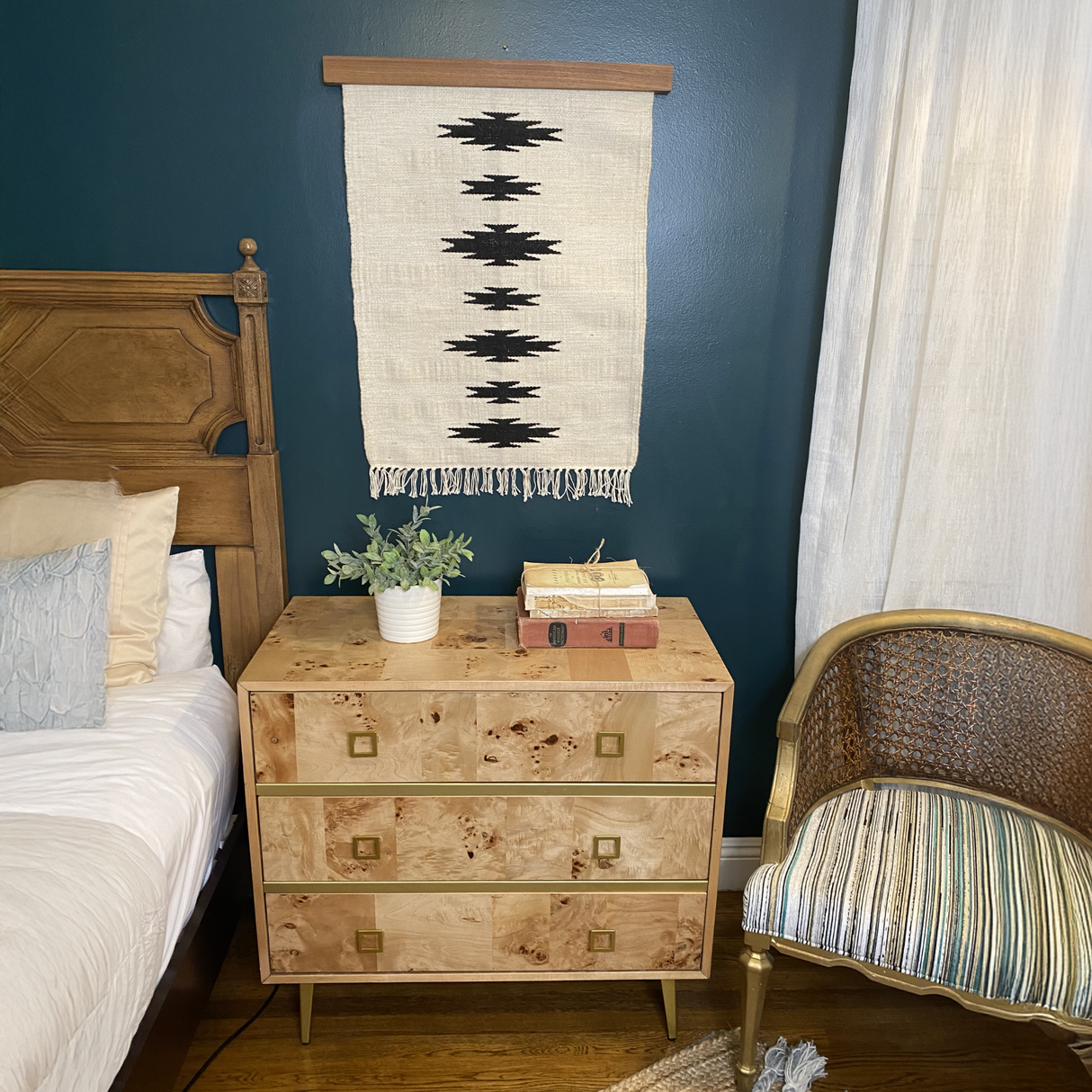 Chysto (Pure) Wool Rug / Wall Hanging, displayed with a Hemlock Wood Rug Hanger ($240 value), alongside books, a potted plant, and gold chair—creating an inviting art ensemble beside the bed.