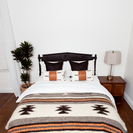 A cozy bed with patterned pillows and the Chysto (Pure) Wool Statement Bed Blanket featuring Ukrainian star symbols, flanked by a plant and a lamp on wooden bedside tables.