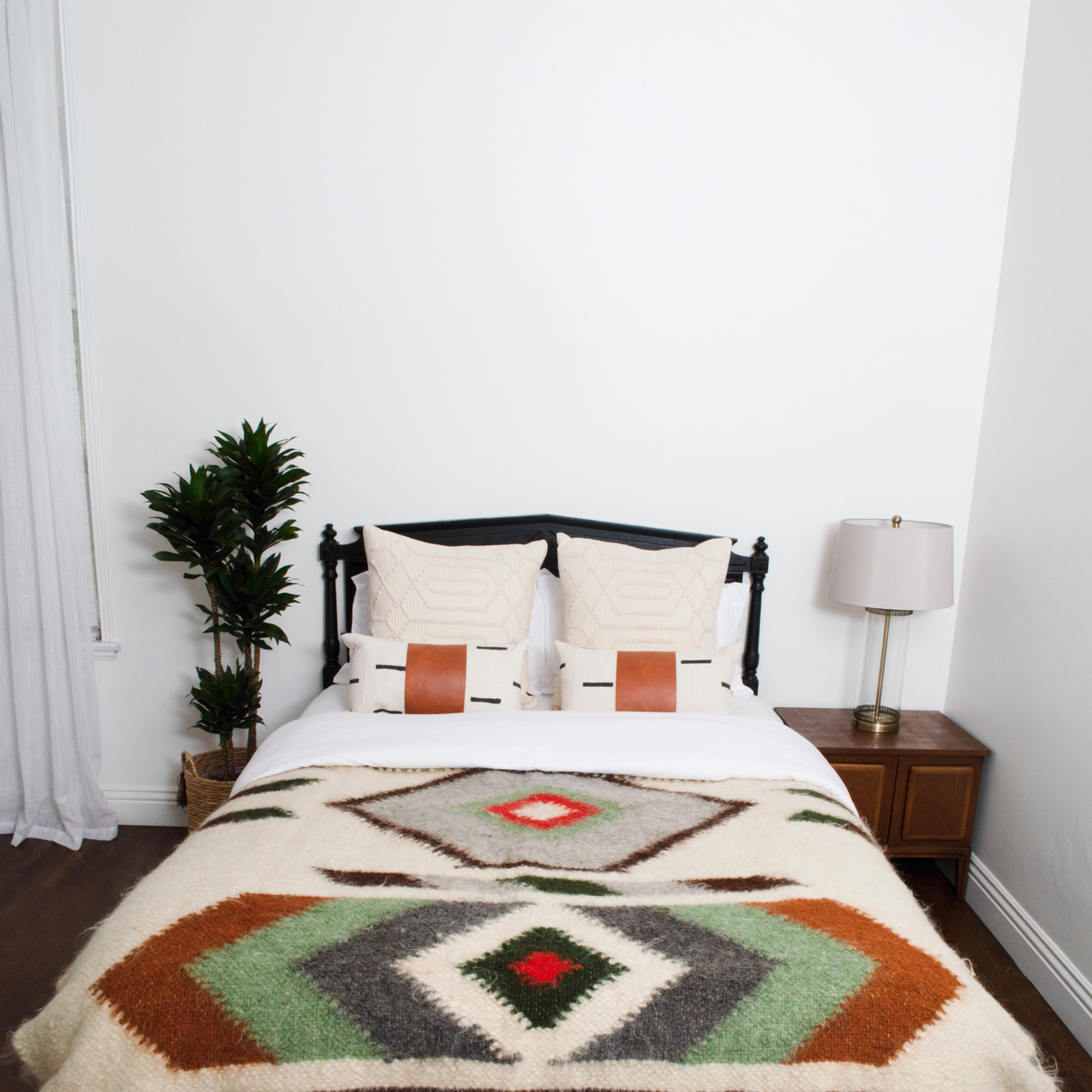 A neatly made bed with the Diamant Wool Statement Bed Blanket, two pillows, a plant, and a lamp on a wooden nightstand brings cozy winter charm to the decor.