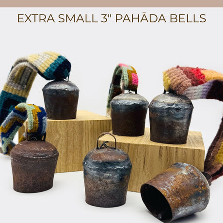 Six vintage handmade Pahāḍa yak, goat & sheep's bells from the Himalayan mountains of Nepal and Tibet, each 3" with colorful straps, displayed on wooden blocks—perfect for Christmas ornaments, wreath decor, or sound bath.