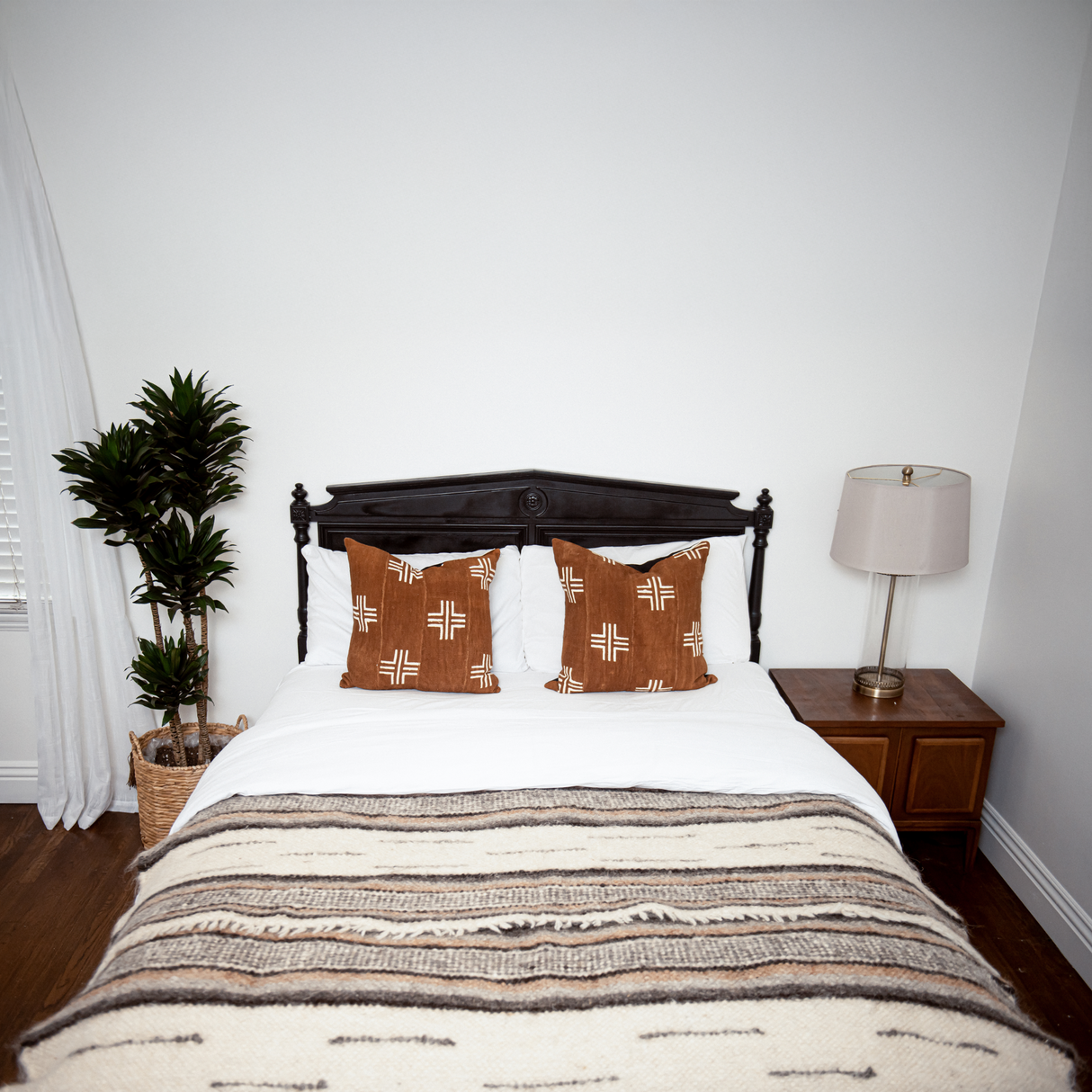 A neatly made bed with decorative pillows, a Gratsia (Grace) Wool Statement Bed Blanket draped over it, a bedside lamp, and a potted plant.